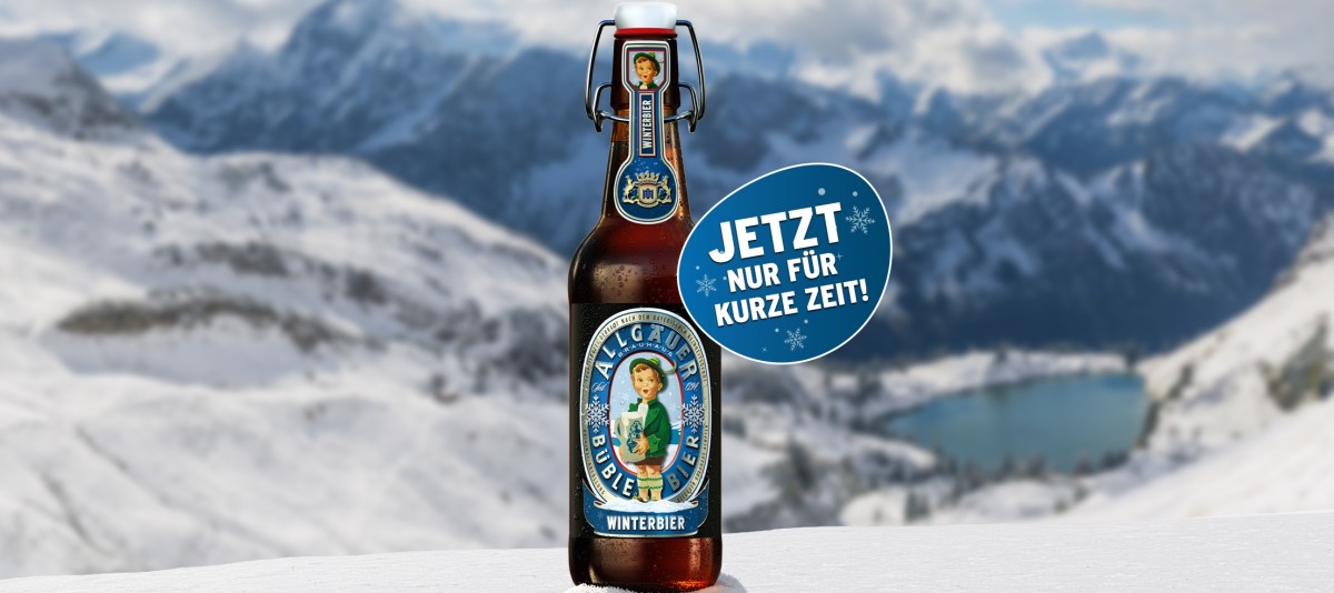 Allgäuer Büble Winterbier Bügelflasche steht im Schnee vor verschneiter Alpenlandschaft mit Bergsee